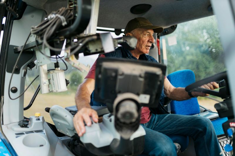Elderly man operating an advance technology tractor on farm. Senior farmer driving a tractor for doing agriculture activities on his farm.