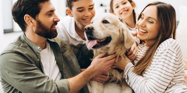 Happy family of four joyfully cuddling their golden retriever dog at home.