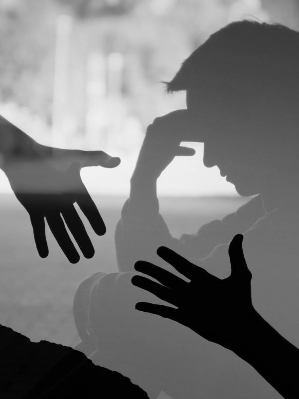 Mental health crisis support- a distressed man sitting down with  shadows of others' hands reaching 