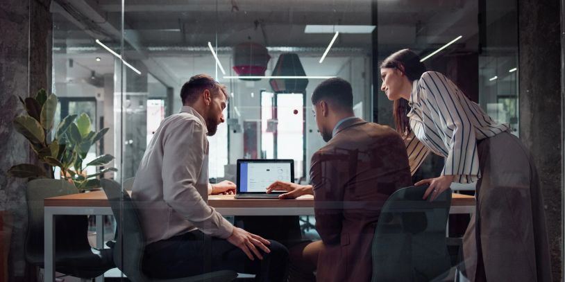 Three colleagues collaborating around a laptop in a modern office.