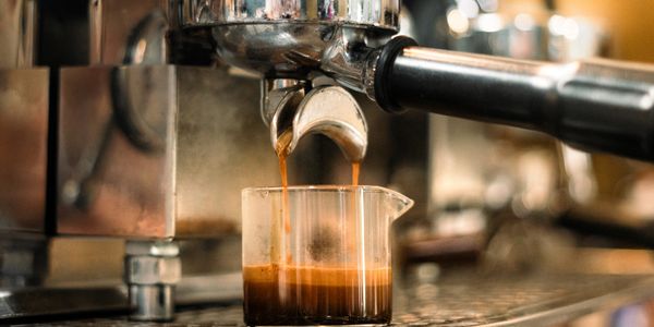 Espresso coffee brewing from an espresso machine into a glass container.