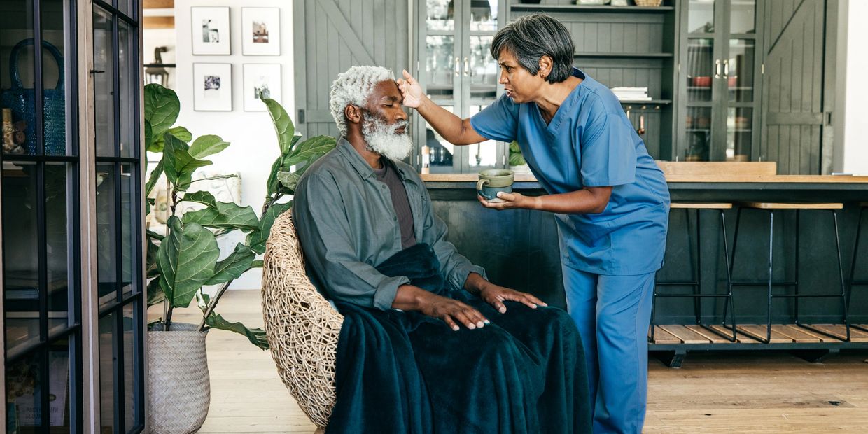 Nurse caring for elderly man in cozy home setting, checking his forehead.