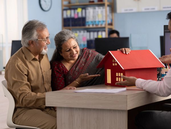 Elderly couple discussing a house model with a real estate agent.