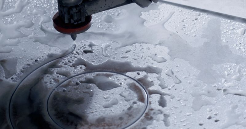 Close-up of a water cutting CNC machine slicing intricate curves into a wet metallic surface, showcasing advanced industrial precision and cutting-edge machinery.
