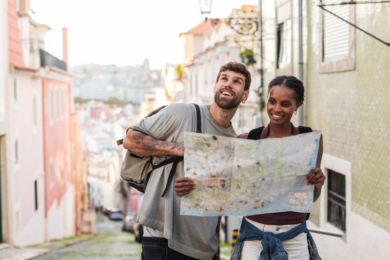Two happy tourists are consulting a map while visiting lisbon, portugal, enjoying their summer vacation and exploring the city's beautiful streets and landmarks