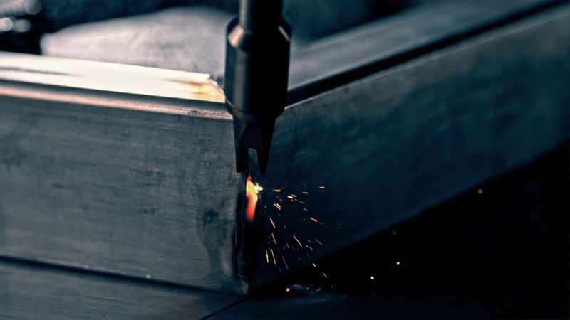 Detailed close-up of aluminum welding in progress, showing bright sparks and metallic textures under focused lighting in an industrial setting.