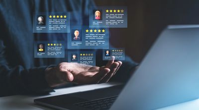 Hand hovering over laptop with floating customer review cards showing star ratings.