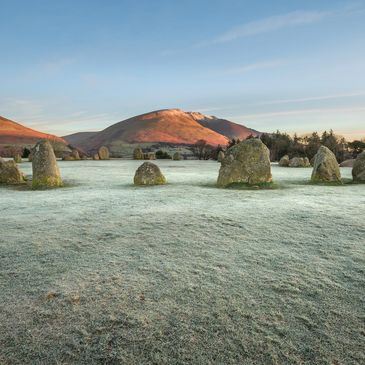 Ancient stone circle on frosted grass with sunrise-lit hills in the background.