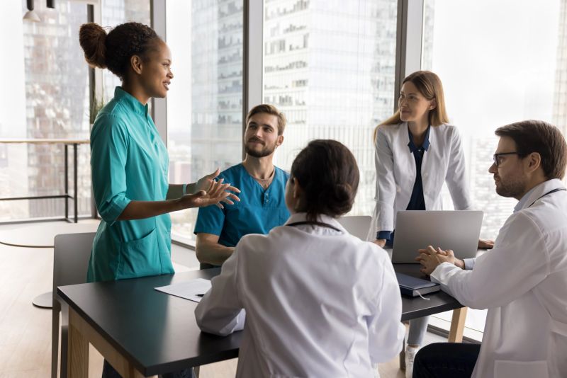 African doctor with colleagues engaged in meeting, briefing event in boardroom, take part in concilium, consulting on complex case, sharing opinions, make diagnosis, determine further treatment option