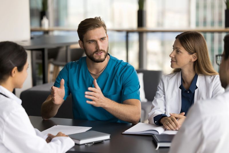 Diverse doctors listening colleague at briefing, gathered together for clinical case review, discussing treatment plan for patients with complex or chronic conditions. Collaborative medical advisory