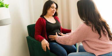 Woman comforting another by holding her stomach.