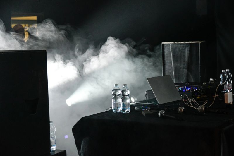 Concert stage before a performance, featuring spotlights, fog machines, speakers, a sound system, and a DJ console. A dynamic event production scene capturing the anticipation of a live show.