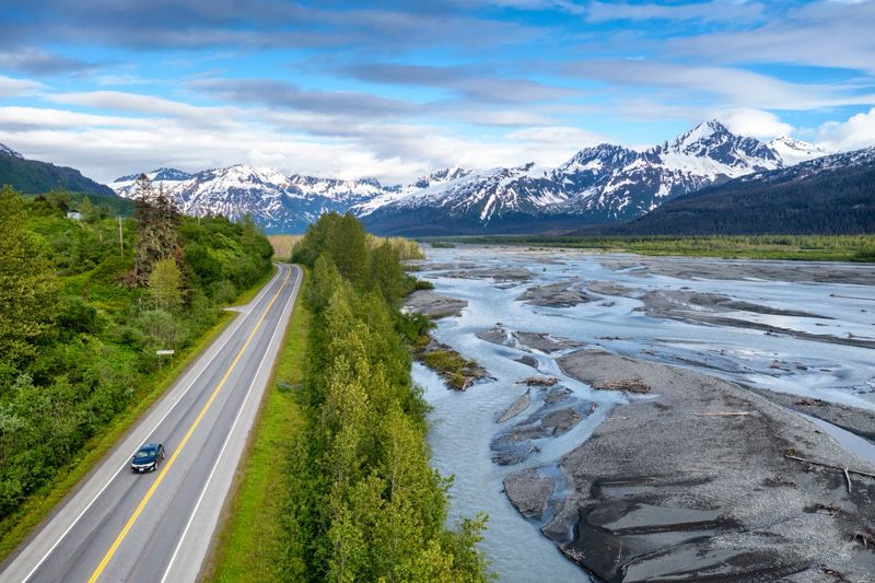 Aerial view of a car on a road leading to a snow capped Mountain range in Alaska
