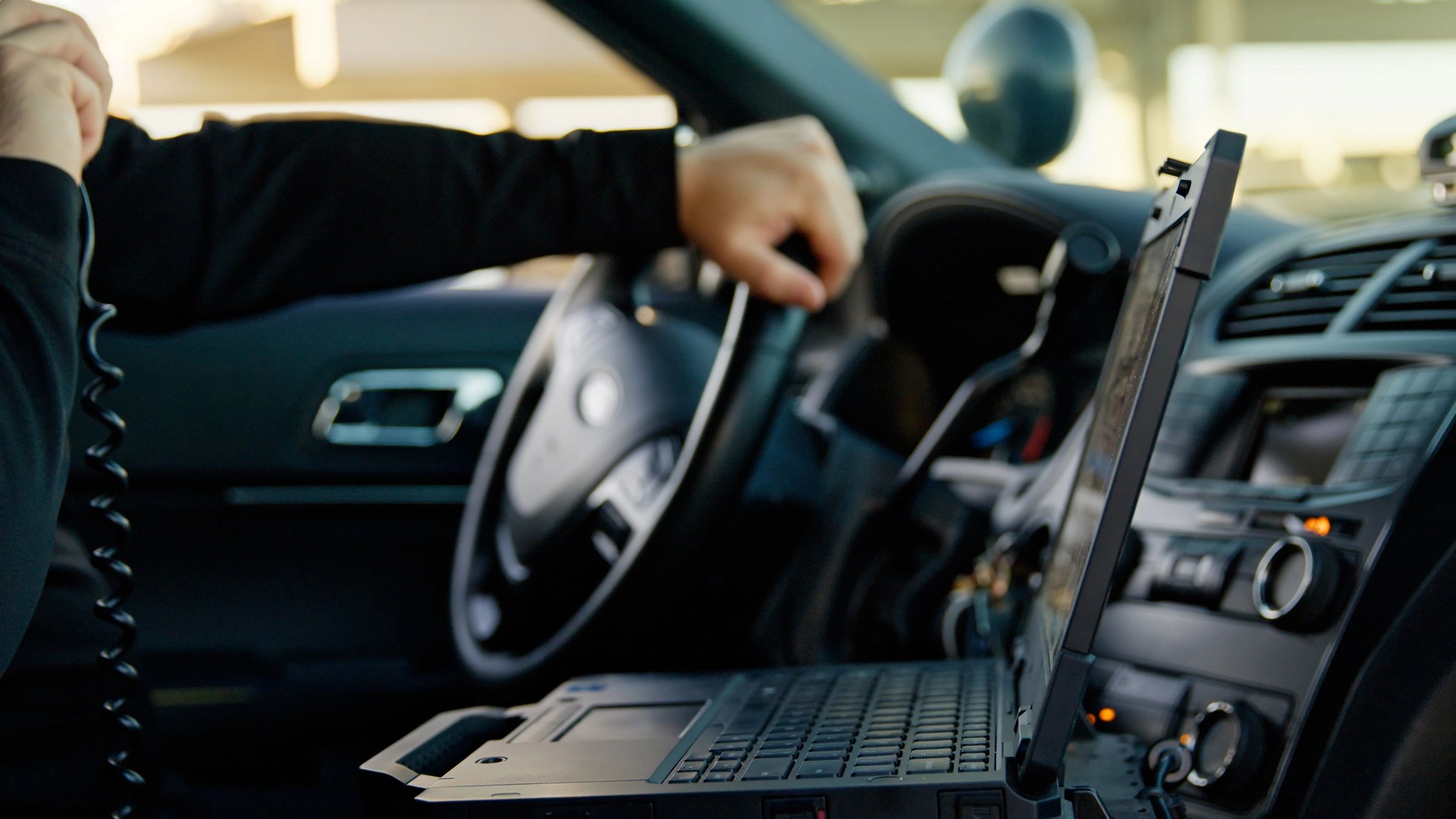 Police officer communicating inside a patrol car with a laptop.