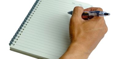 Hand holding pen poised over a blank spiral notebook page.