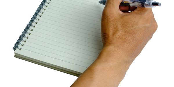 Hand holding pen poised over a blank spiral notebook page.