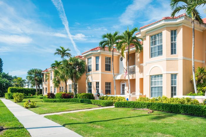 Sunlit peach-colored townhouse with palm trees and manicured lawns under a clear blue sky.