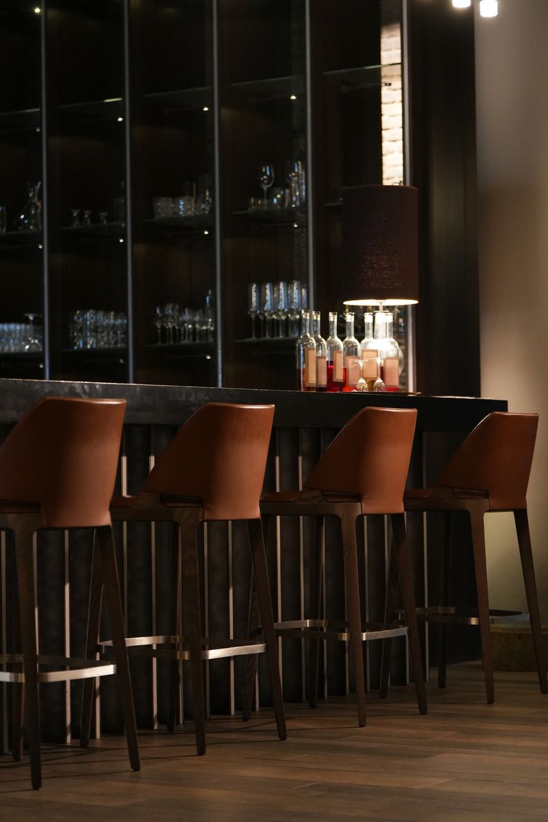 A row of bar stools lined up against a sleek bar counter with illuminated shelves displaying glassware and bottles