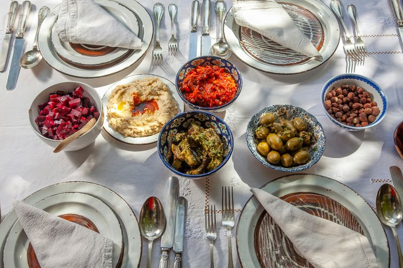 Beautifully arranged table showcasing a variety of colorful moroccan dishes like hummus, beetroot salad, olives, and roasted vegetables, inviting shared meals