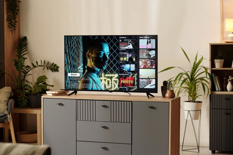 TV on cabinet displaying various video thumbnails in modern living room setting with plants and decorative items. Home ambiance giving relaxing and inviting atmosphere