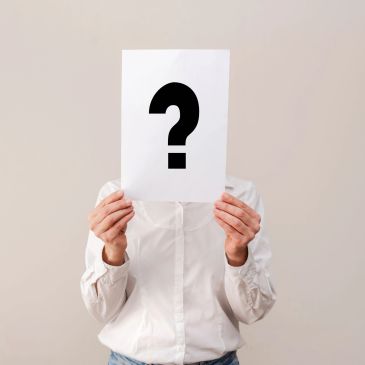 Person holding paper with question mark covering face.