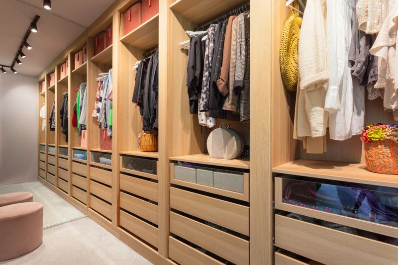 A modern elegant walk-in closet with oak wood cabinets and drawers, spotlights and a mirror.