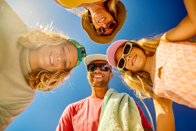 Cheerful family forming a circle and smiling at the camera during summer vacation at an australian beach