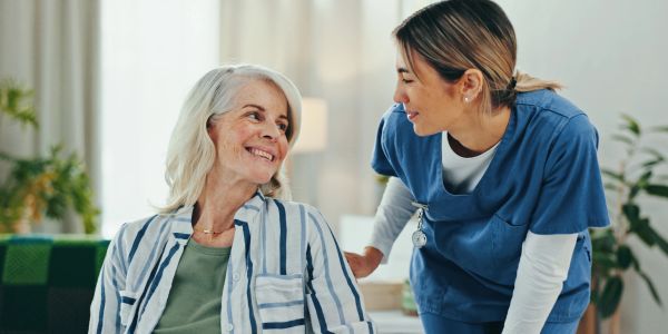 Elderly woman smiling at nurse in blue scrubs.