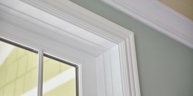 Close-up of white window trim and crown molding on a light gray wall.
