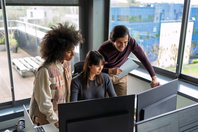 Software engineers collaborating, analyzing code on desktop monitors within minimalist corporate workspace, teamwork driving technological innovation