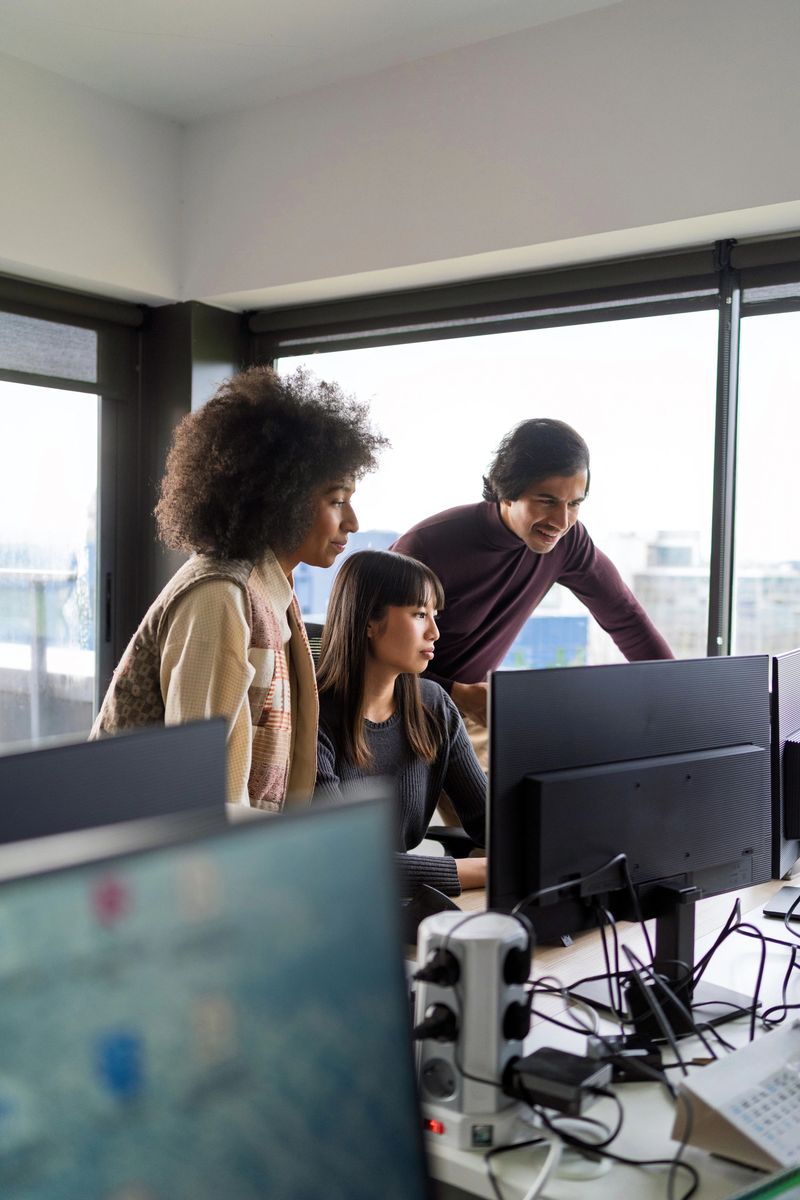Team of software developers working together, analyzing code and brainstorming solutions in contemporary workspace with multiple computer screens