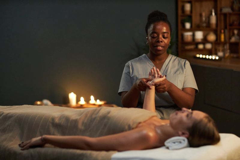 Massage therapist providing relaxing treatment to a client on massage table in serene, candle-lit room with wellness products surrounding