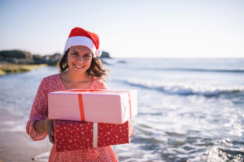 Portrait of woman with Christmas hat and Christmas presents at the beach.