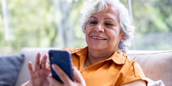 Smiling elderly woman using a smartphone on a cozy couch.