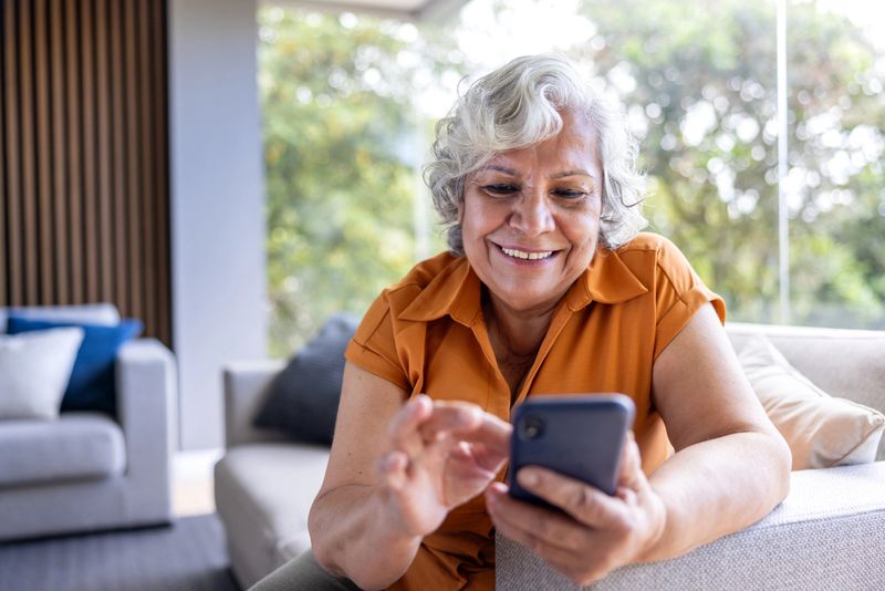 Happy Latin American senior woman smiling while using her cell phone at home - lifestyle concepts
