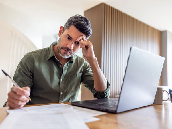 A man looks stressed while working with papers and a laptop.