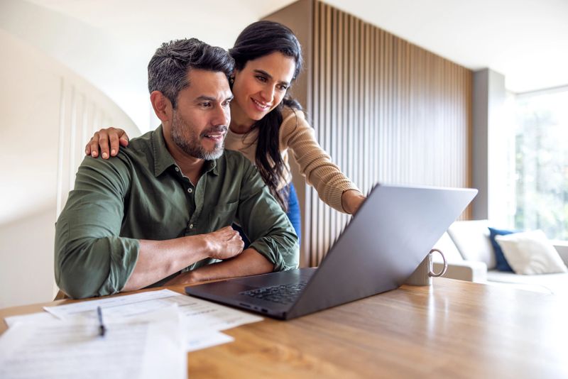 Loving couple organizing their home finances and looking at bank statements while using their laptop - financial planning concepts