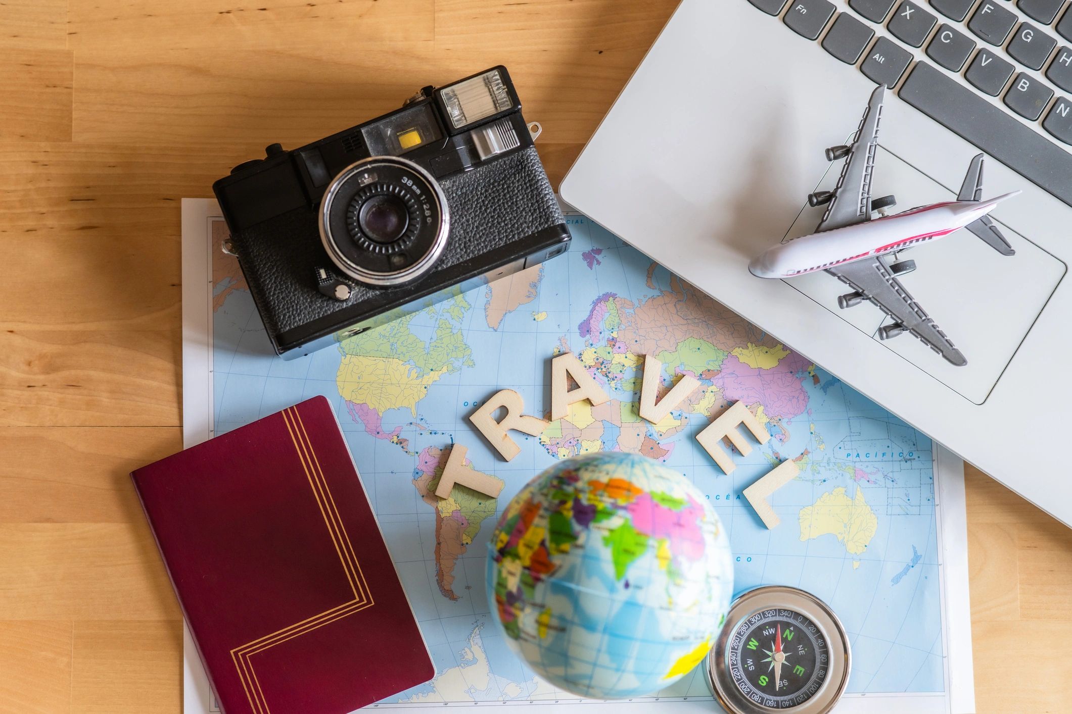 Travel essentials on a world map: camera, passport, globe, compass, and toy plane.