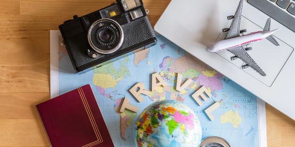 Travel essentials including a camera, globe, passport, compass, and toy airplane on a map.