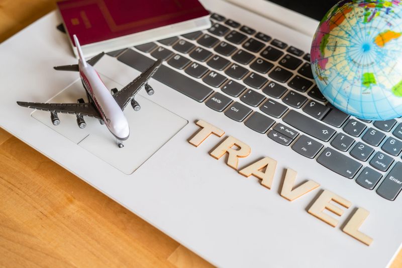 Airplane model, passport, globe and wooden letters spelling travel are laying on laptop keyboard suggesting online booking and vacation trip planning
