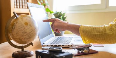 Person pointing at laptop screen beside a globe.