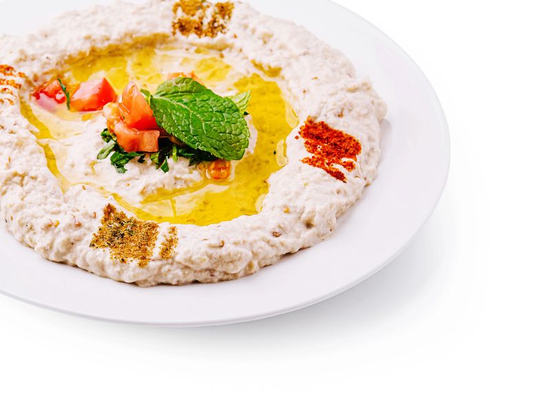 A bowl of creamy hummus is drizzled with olive oil and garnished with fresh mint, tomatoes, and vibrant spices. Ideal for sharing at gatherings or enjoying as a snack.