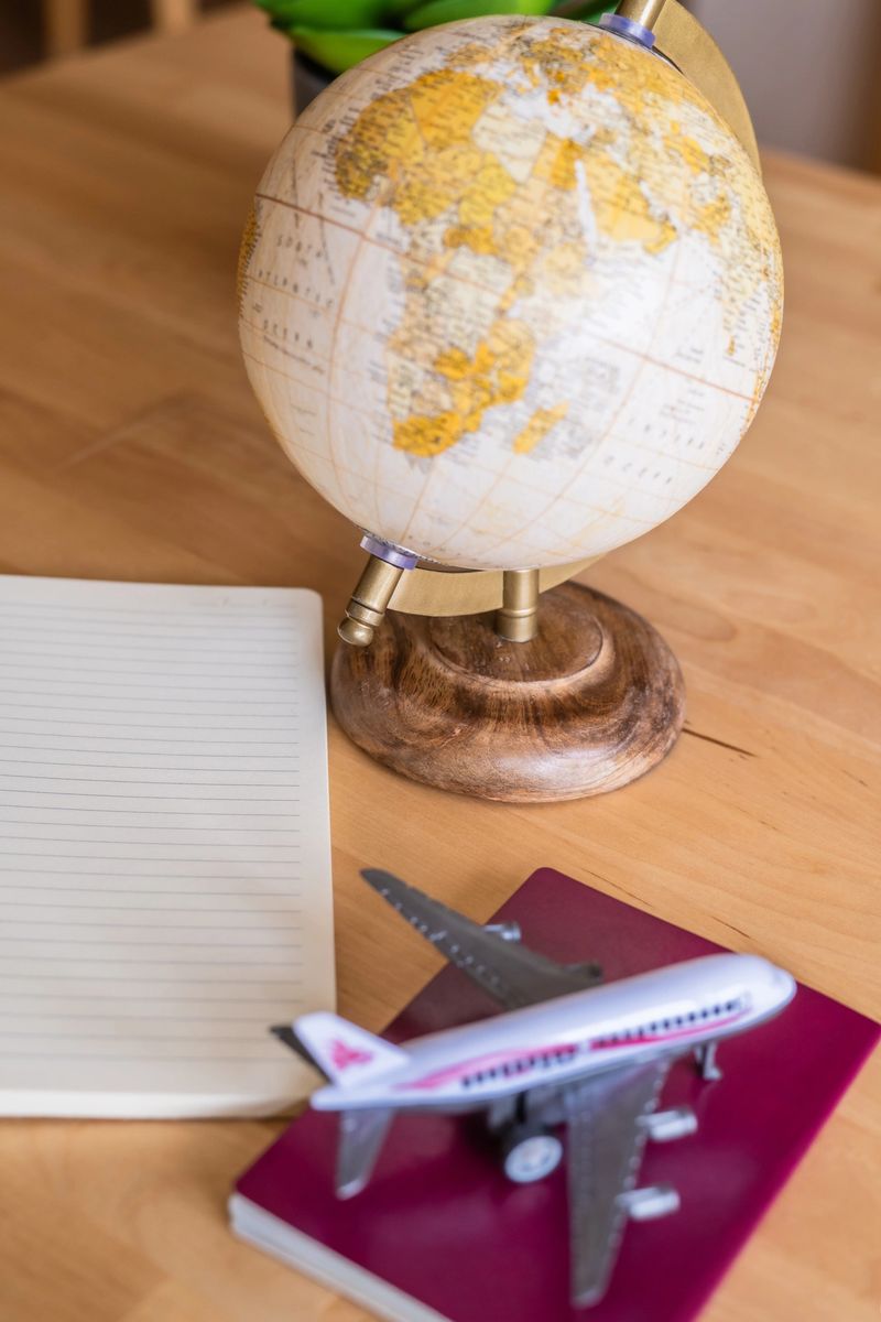 Globe, passport, toy airplane and notebook laying on a wooden table suggest upcoming travel arrangements for a pleasant trip around the world