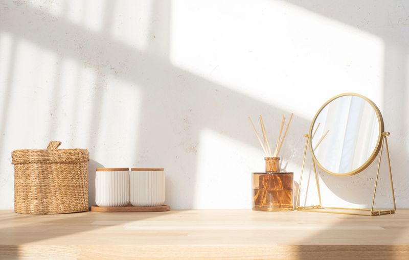 Dressing table top with round mirror, aroma sticks and containers on blurred abstract texture wall background in soft window sunlight shadows