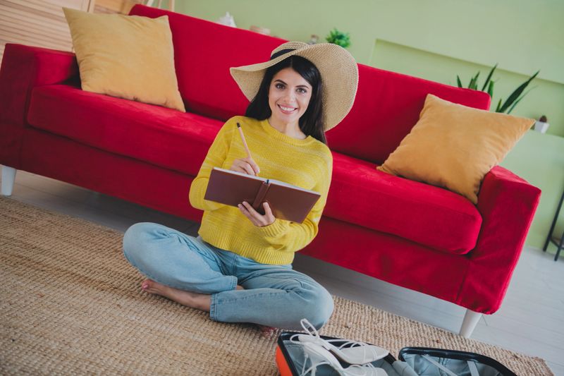 Charming woman in casual attire seated on a rug in her inviting living space, jotting down thoughts in a notebook, embracing a peaceful moment.