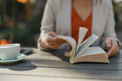 Person reading a book outdoors with a cup of coffee on the table.