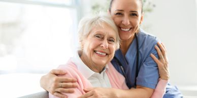 Elderly woman and nurse smiling and hugging.