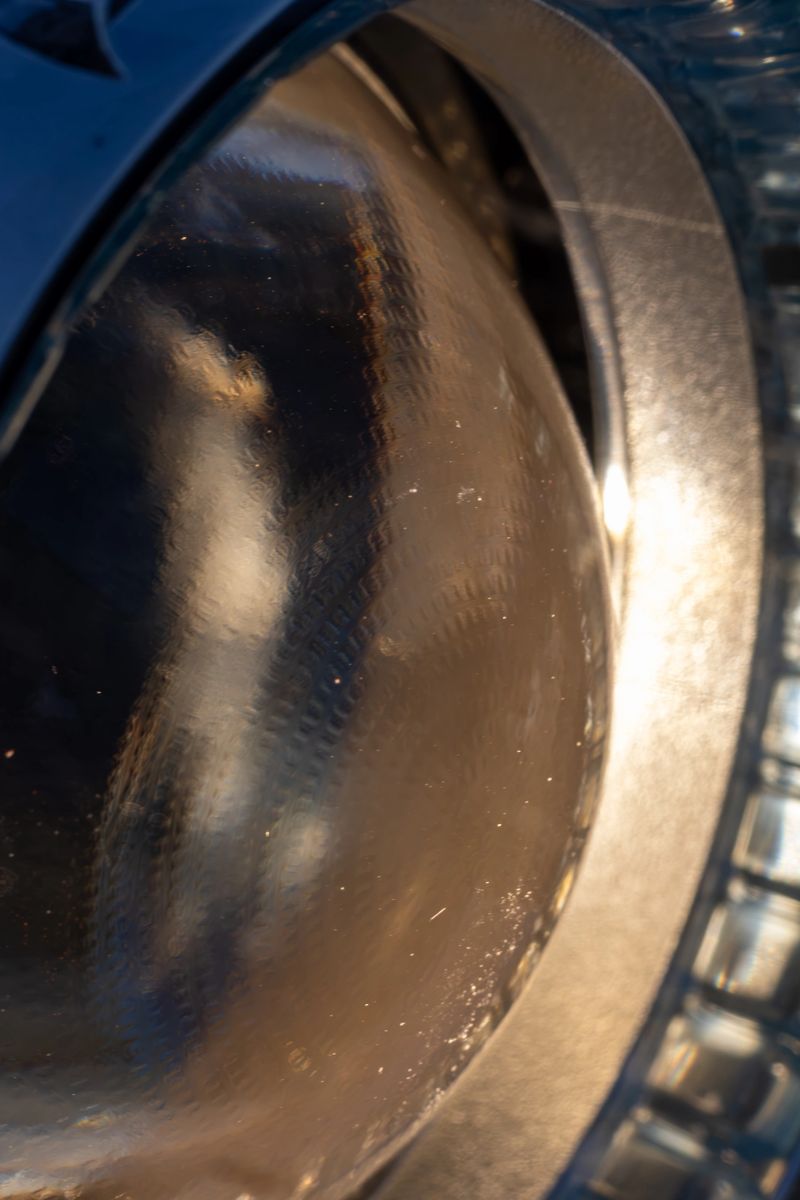 A macro shot of a reflective glass surface, possibly a vehicle headlight, with warm light reflections. The intricate details and metallic textures create an abstract and futuristic aesthetic. The interplay of light and shadow enhances the depth and complexity of the image.