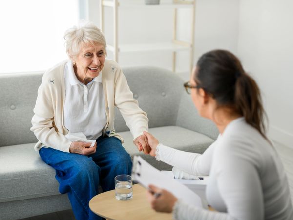 Elderly woman smiling and holding hands with a therapist during a session.