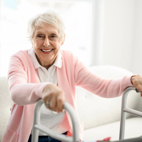 Smiling elderly woman using a walker indoors.